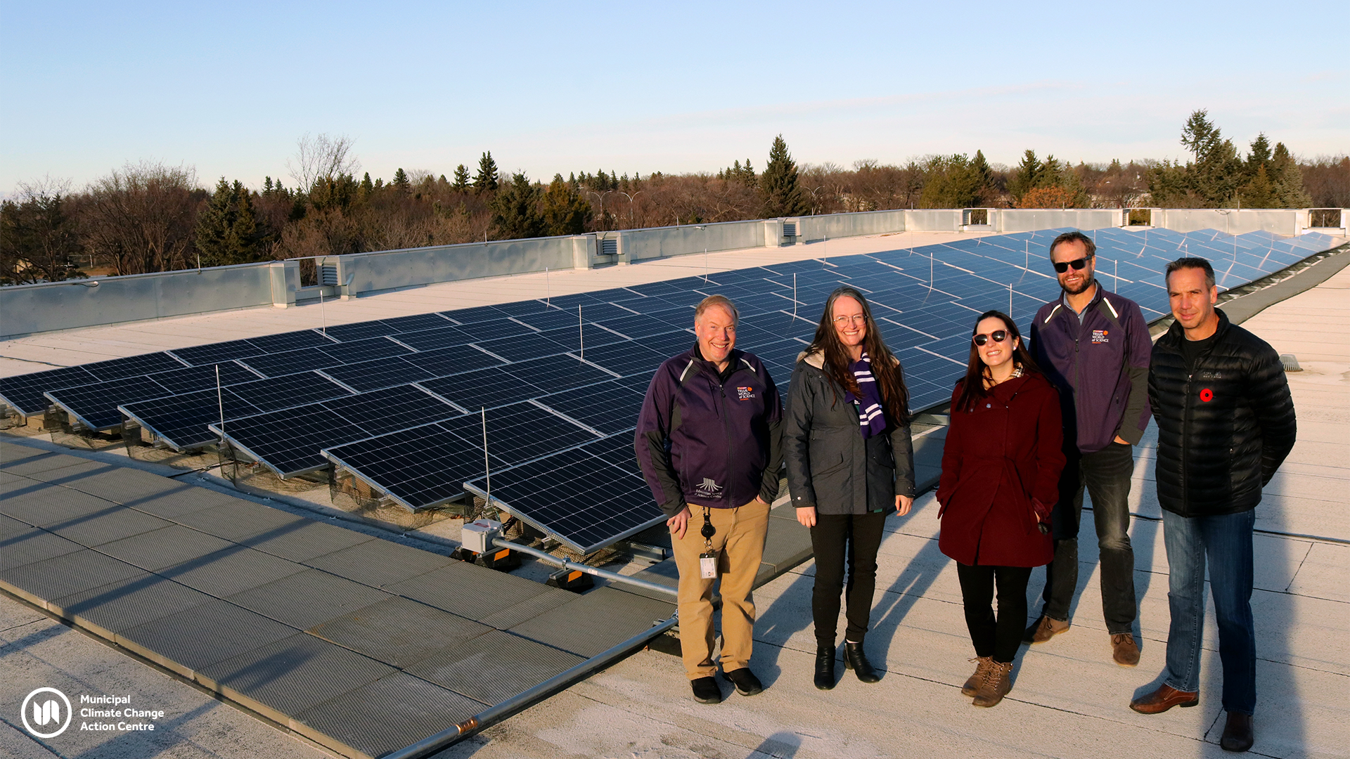 Five adults stand in front of rooftop solar panels in Edmonton